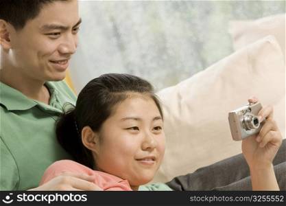 Close-up of a young woman holding a camera with a young man looking at it
