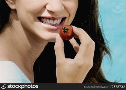 Close-up of a young woman holding a cherry tomato and smiling