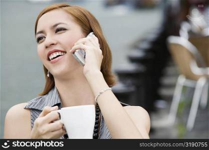 Close-up of a young woman holding a coffee cup and talking on a mobile phone