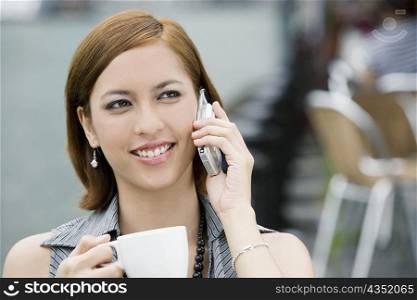 Close-up of a young woman holding a coffee cup and talking on a mobile phone