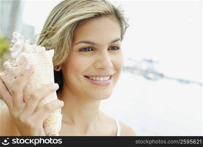 Close-up of a young woman holding a conch shell and smiling
