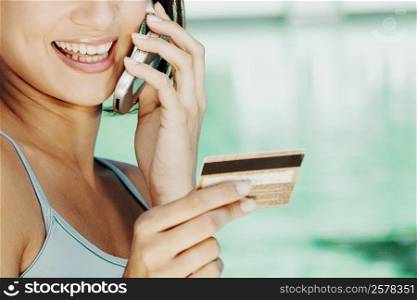 Close-up of a young woman holding a credit card and talking on a mobile phone