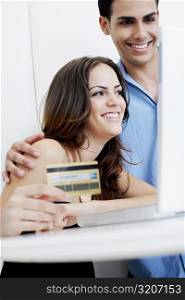 Close-up of a young woman holding a credit card with a young man looking at a laptop