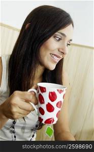 Close-up of a young woman holding a cup of tea and smiling