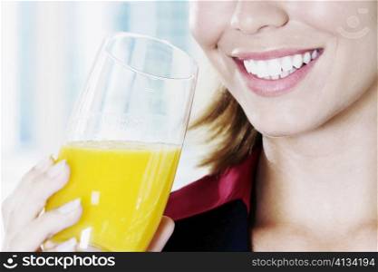 Close-up of a young woman holding a glass of orange juice and smiling