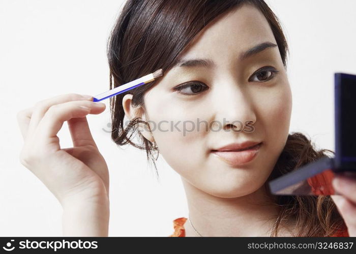 Close-up of a young woman holding a make-up brush and a hand mirror