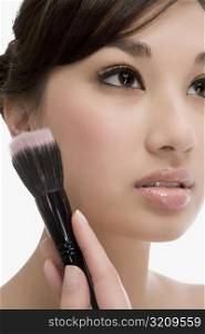 Close-up of a young woman holding a make-up brush and thinking