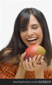 Close-up of a young woman holding a mango and laughing