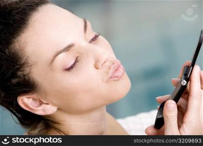 Close-up of a young woman holding a mobile phone and blowing a kiss