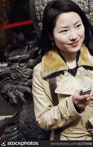 Close-up of a young woman holding a mobile phone looking away