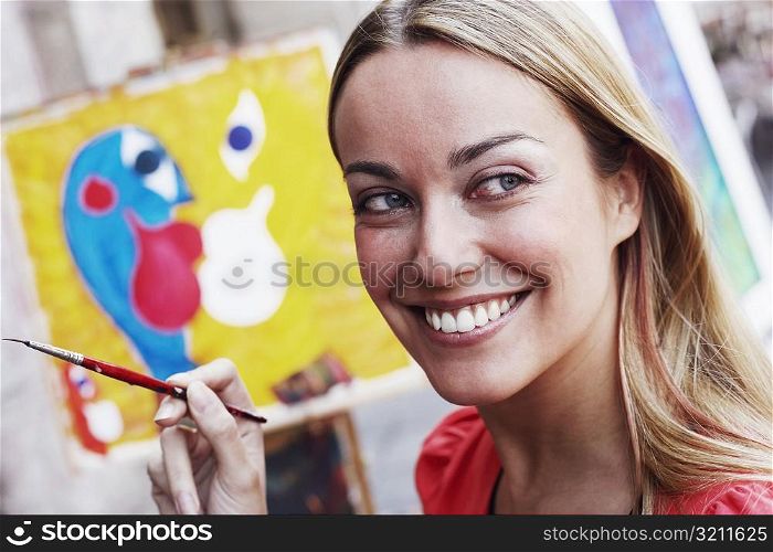 Close-up of a young woman holding a paintbrush and smiling