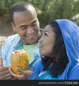 Close-up of a young woman holding a pineapple beside a mid adult man