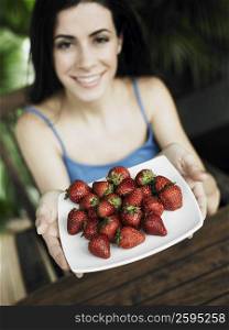 Close-up of a young woman holding a plate of strawberries