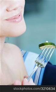 Close-up of a young woman holding a slice of cucumber with a fork