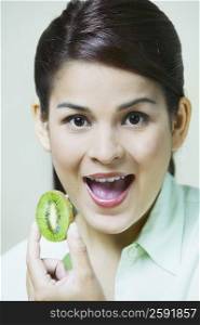 Close-up of a young woman holding a slice of kiwi fruit