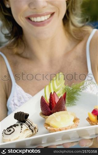 Close-up of a young woman holding assorted tarts with an eclair in a platter