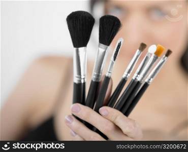 Close-up of a young woman holding make-up brushes