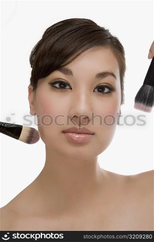 Close-up of a young woman holding make-up brushes and applying make-up