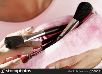 Close-up of a young woman holding make-up brushes in a purse