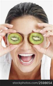 Close-up of a young woman holding slices of kiwi fruit in front of her eyes and laughing