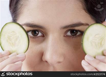 Close-up of a young woman holding two cucumber slices
