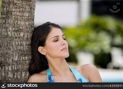 Close-up of a young woman leaning against a tree and thinking