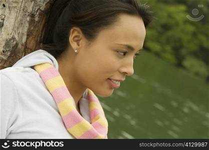 Close-up of a young woman leaning against a tree trunk