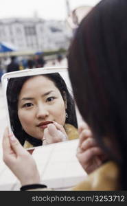 Close-up of a young woman looking into a mirror applying lipstick