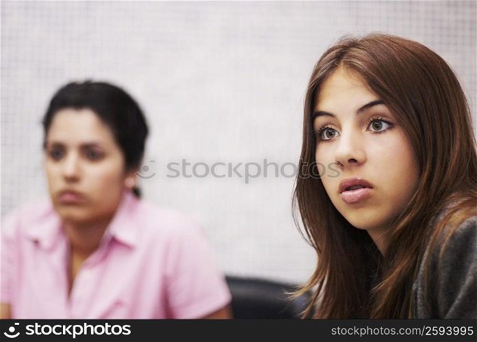 Close-up of a young woman looking surprised with another young woman in the background