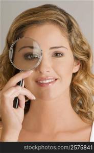 Close-up of a young woman looking through a magnifying glass
