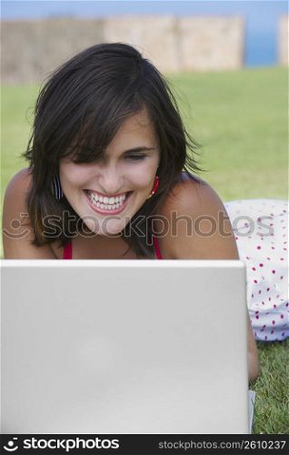 Close-up of a young woman lying in a lawn in front of a laptop