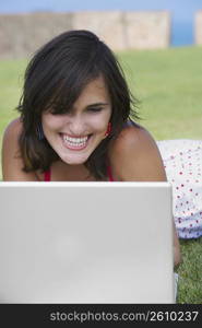 Close-up of a young woman lying in a lawn in front of a laptop