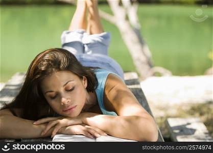 Close-up of a young woman lying on a bench reading a book