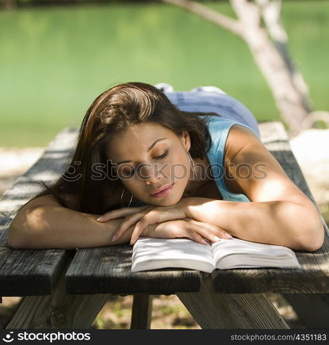 Close-up of a young woman lying on a bench reading a book