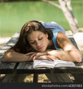 Close-up of a young woman lying on a bench reading a book