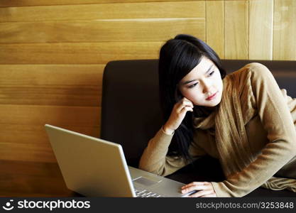 Close-up of a young woman lying on a couch in front of a laptop