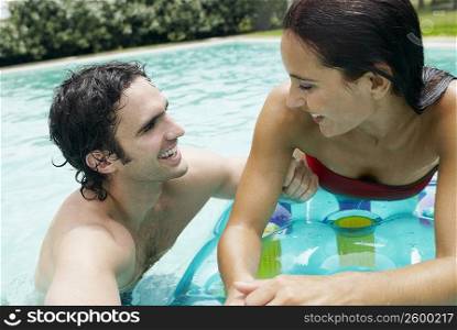 Close-up of a young woman lying on a pool raft and looking at a young man