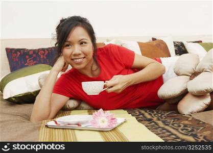 Close-up of a young woman lying on the bed and holding a cup of tea