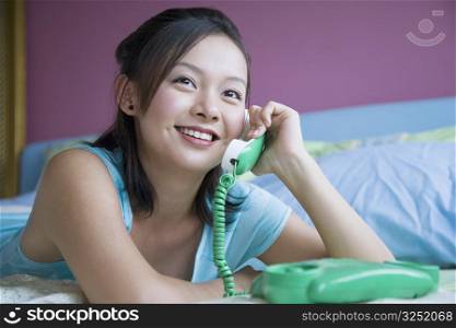Close-up of a young woman lying on the bed and talking on the telephone