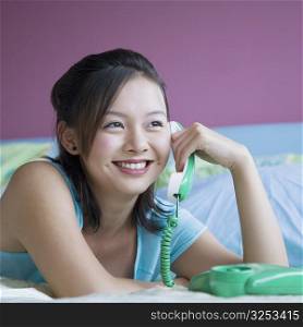 Close-up of a young woman lying on the bed and talking on the telephone