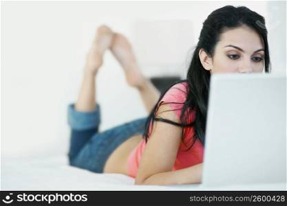 Close-up of a young woman lying on the bed and using a laptop