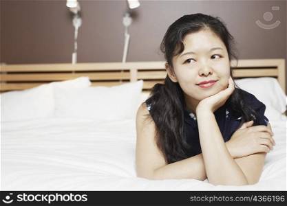 Close-up of a young woman lying on the bed thinking with her hand on her chin