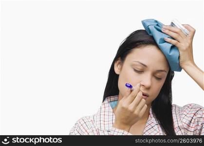 Close-up of a young woman measuring her temperature with a thermometer and holding an ice pack on her head