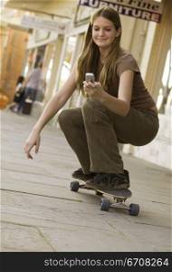 Close-up of a young woman on a skateboard and looking at a mobile phone