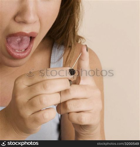 Close-up of a young woman pinching her finger with a needle