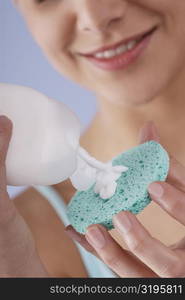 Close-up of a young woman pouring moisturizer on a sponge