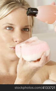 Close-up of a young woman pouring soap on a bath sponge