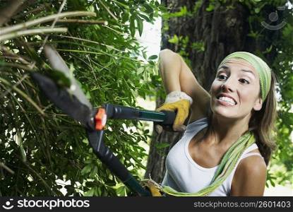Close-up of a young woman pruning a hedge with hedge clippers