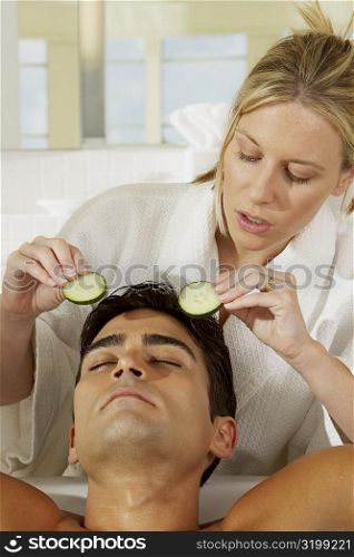 Close-up of a young woman putting cucumber slices on a young man&acute;s eye