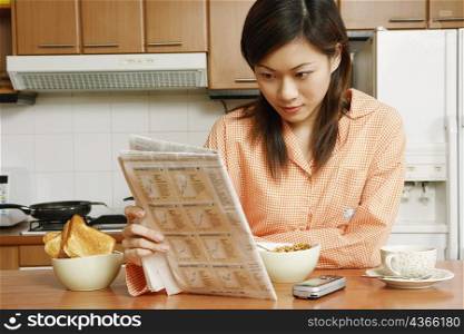 Close-up of a young woman reading a newspaper at a kitchen counter